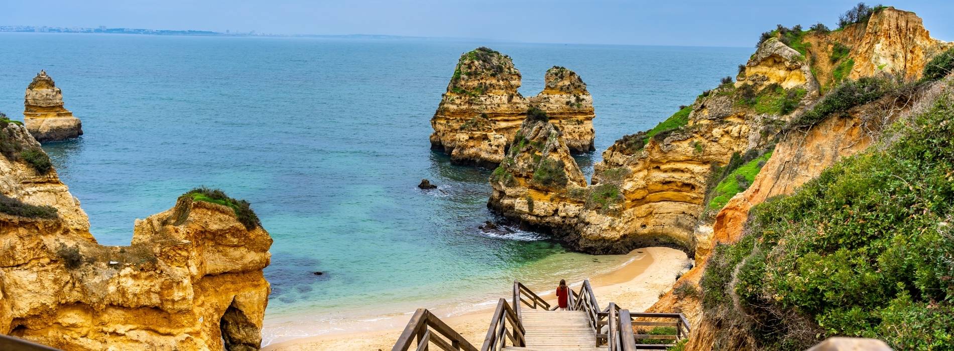 Küste der Algarve mit goldenen Felsformationen, türkisblauem Wasser und Treppenweg hinunter zu einer kleinen Bucht.