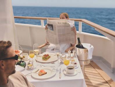 Gäste genießen ein Frühstück an einem gedeckten Tisch an Deck eines Kreuzfahrtschiffs mit Blick auf das offene Meer