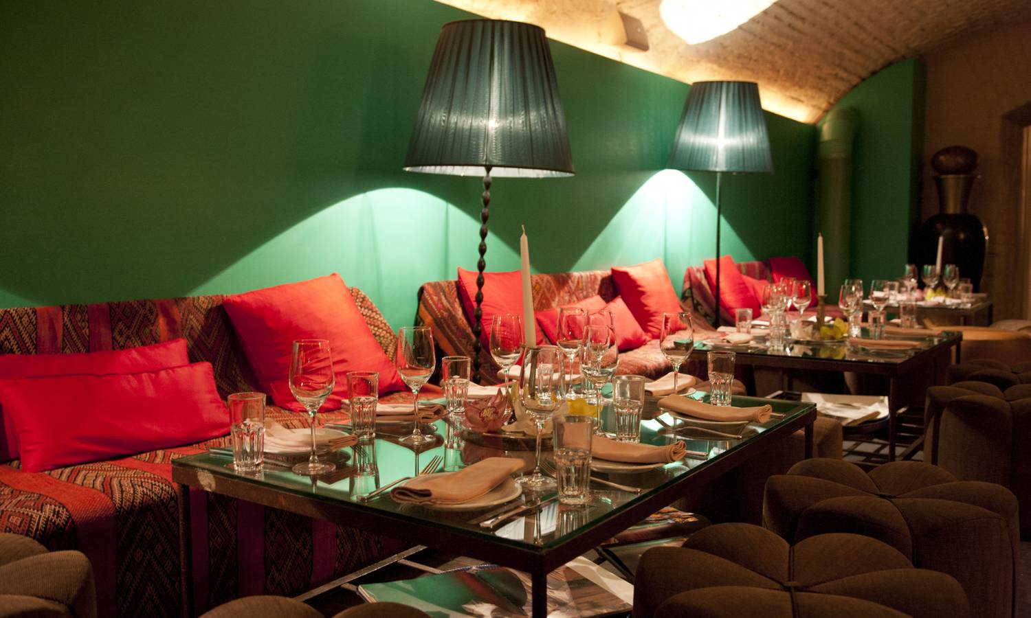 Ein gedimmt beleuteter Raum mit türkiser Wandfarbe. Darin befinden sich roten Sitzgarnituren und festlich gedeckte Tische.