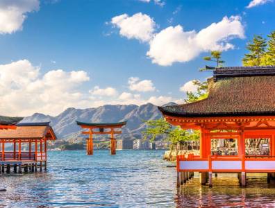 Schwimmendes Torii des Itsukushima-Schreins in Hiroshima mit traditionellen Gebäuden, Meer und Bergen im Hintergrund