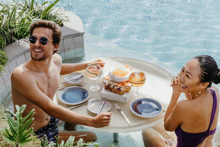Ein Pärchen sitzt fröhlich an der Poolbar und lässt sich ihr Frühstück sichtlich schmecken.