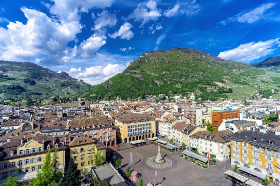 Panoramaansicht von Bozen mit dem Waltherplatz im Zentrum, umgeben von traditionellen Gebäuden und grünen Hügeln unter blauem Himmel.