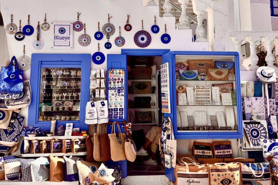 Traditioneller Souvenirladen in Mykonos mit Nazar-Amuletten, handgefertigten Taschen und buntem Schmuck im typischen Blau-Weiß.