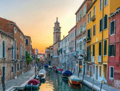 Romantischer Blick auf einen Seitenkanal in Venedig mit bunten Häuserfassaden und Booten bei warmem Abendlicht.