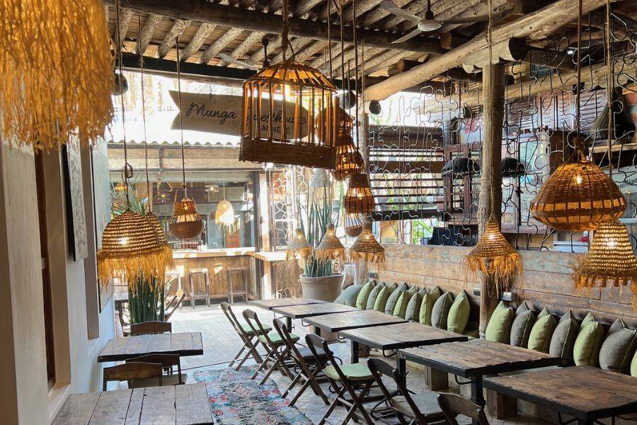 Ein gemütliches Café mit rustikalem Interieur, ausgestattet mit Holztischen, Bambuslampen und handgefertigten Deko-Elementen. Die warme Beleuchtung und die bequemen Sitzkissen verleihen dem Raum eine entspannte, einladende Atmosphäre.