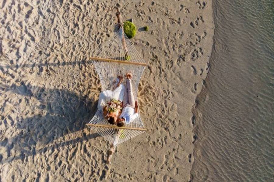 Das Brautpaar - von oben fotografiert - liegt in einer Hängematte am Strand und sieht sich verliebt an.
