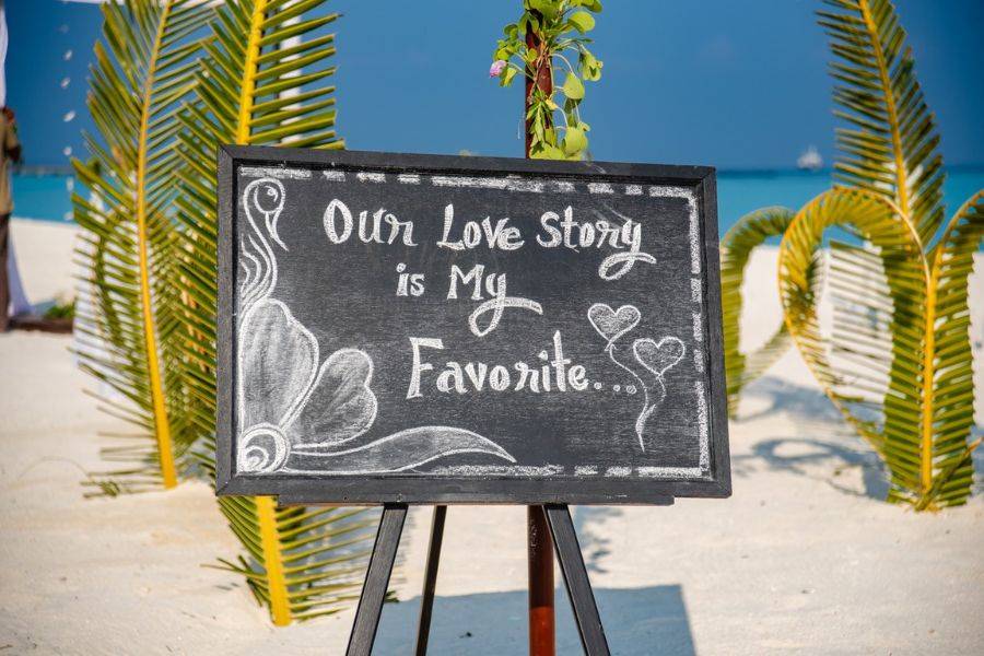 Hochzeitsdekoration am Strand der Malediven mit Schild „Our Love Story is my Favorite“.