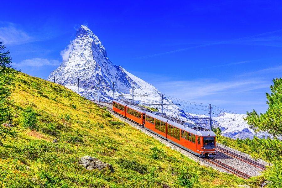 Roter Panoramazug fährt durch die Schweizer Alpen mit Blick auf das Matterhorn bei klarem Himmel
